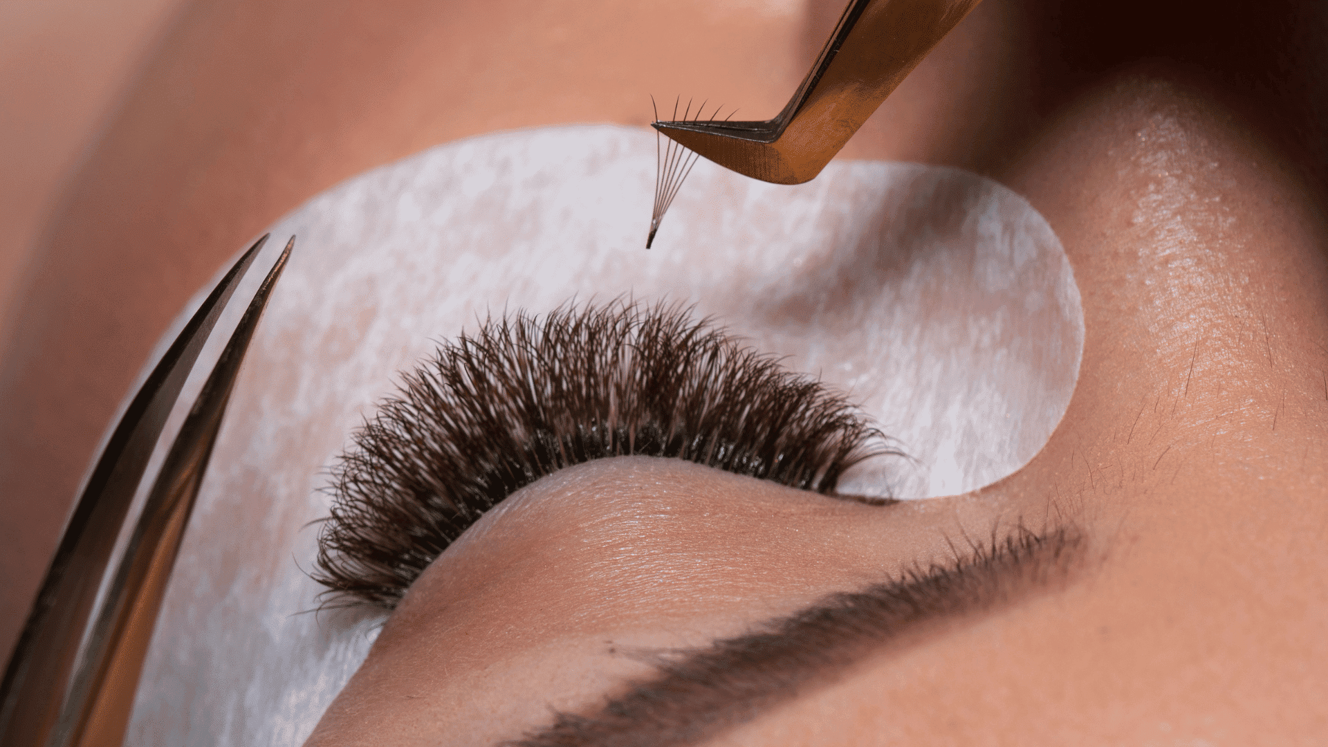 Eyelash extensions being applied with tweezers on a closed eye.