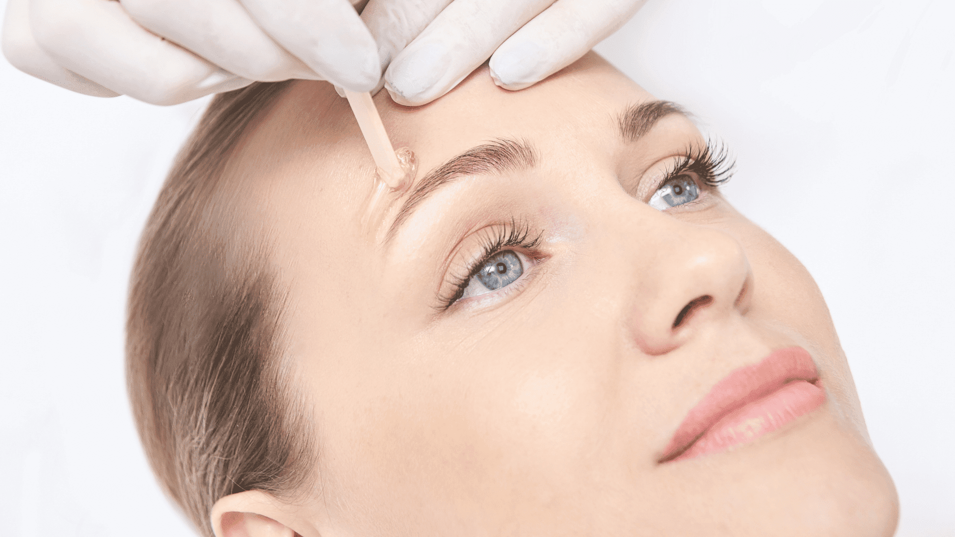 A person receiving a facial treatment with a wooden stick near the eyebrows.
