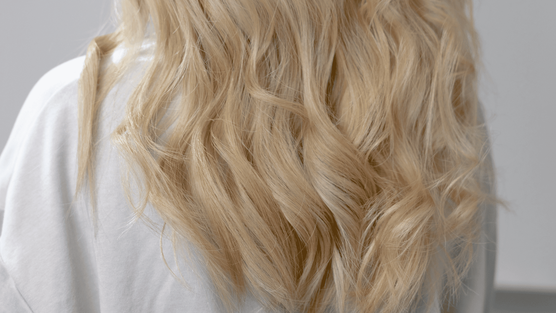 Blonde, wavy hair shown from behind against a neutral background.