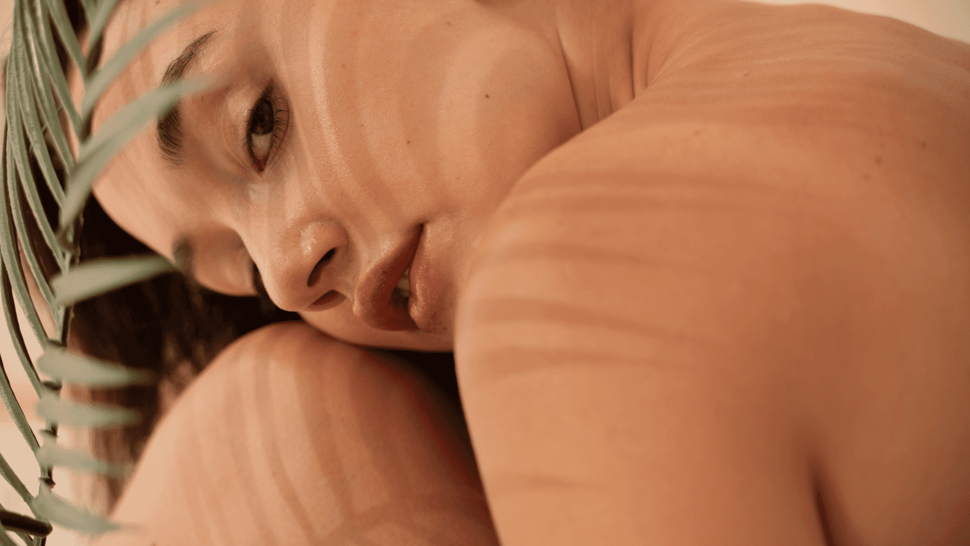 Close-up of a woman's face with leaf shadows on skin, evoking a natural, serene mood.