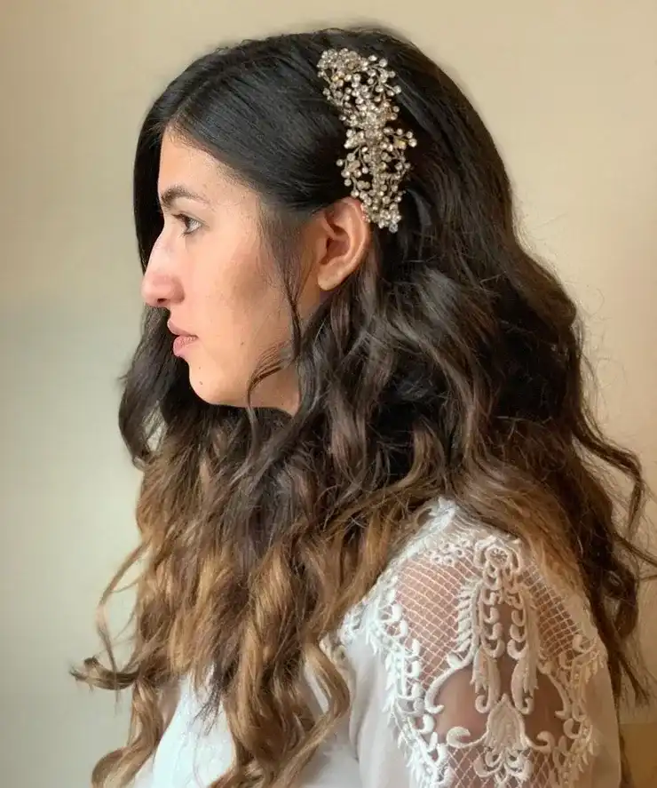 Young woman with wavy hair and ornate hair accessory, wearing a lace-sleeved top.